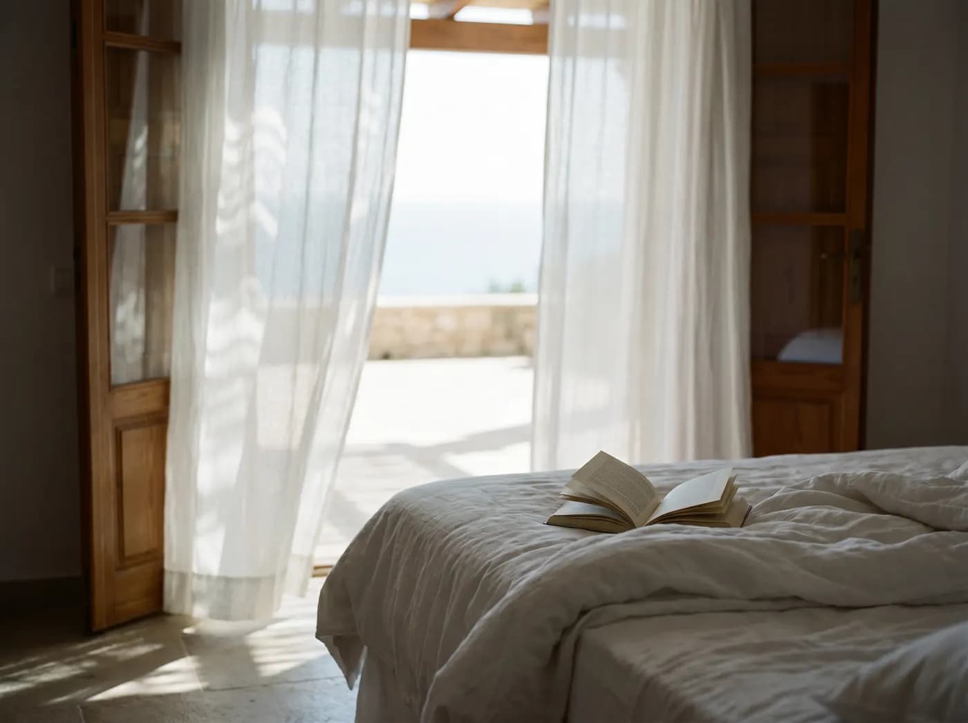 Sheer linen curtains breathing at open doors, the room cool against the bright afternoon
