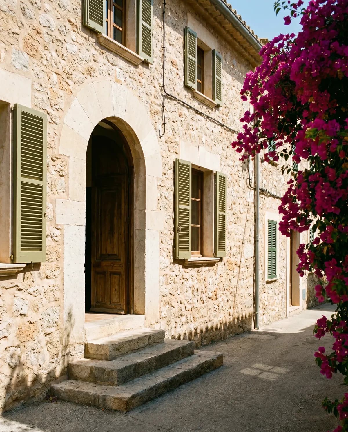 A restored stone house with an arched doorway holding cool shade, steps worn smooth