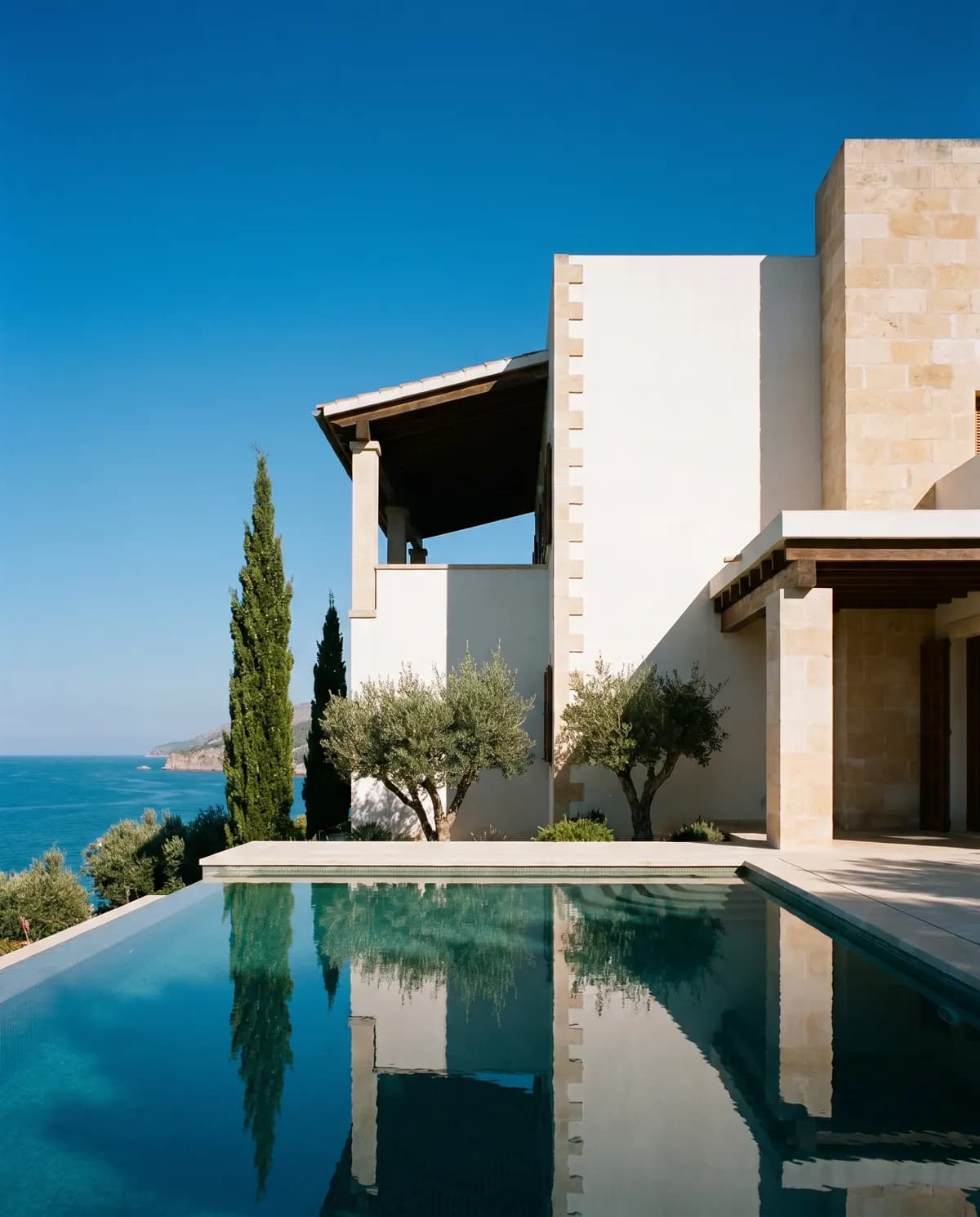 A contemporary white coastal villa in late-morning light, its pool edge meeting the sea